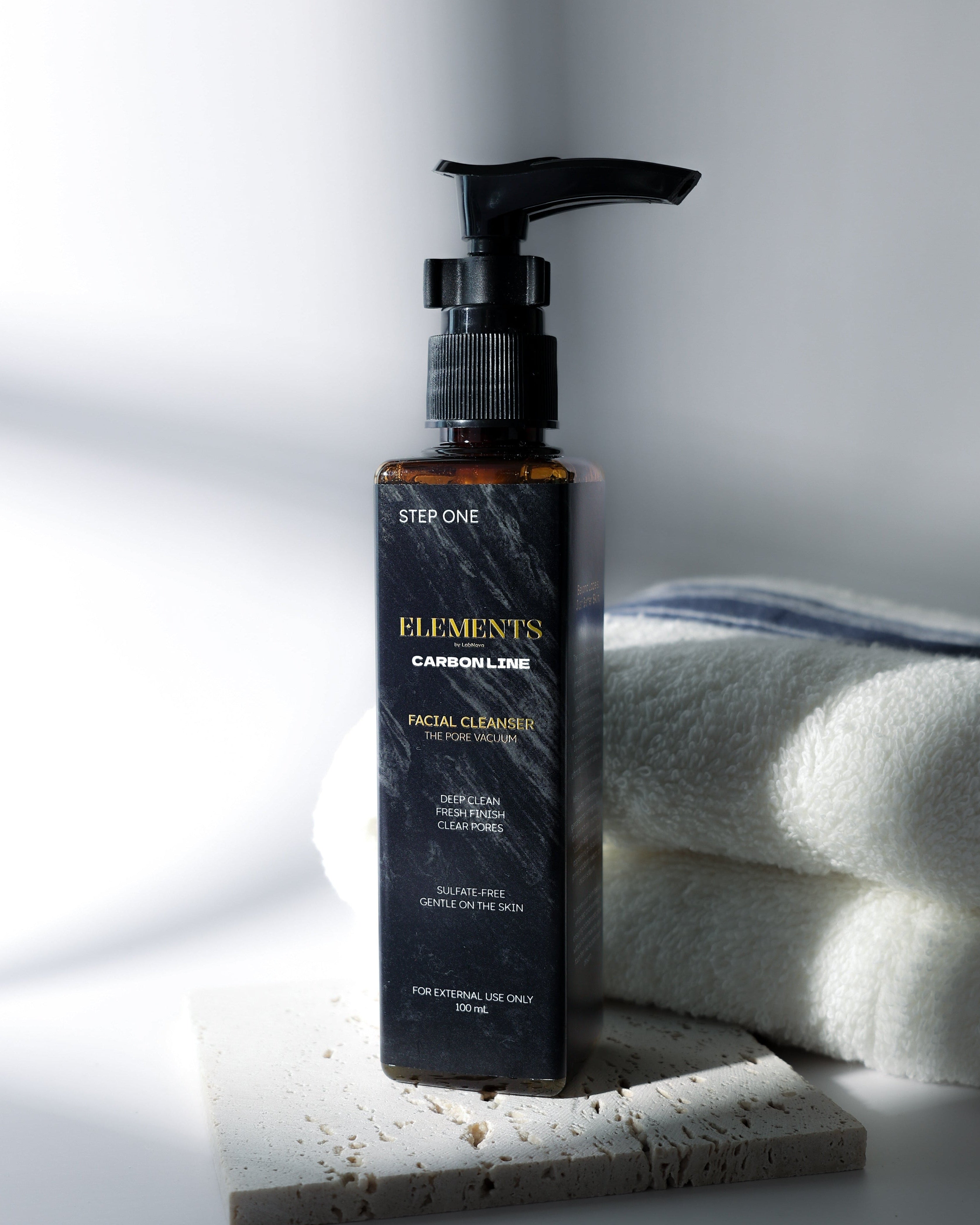 Facial cleansing bottle with pump on a light surface with a towel in the background