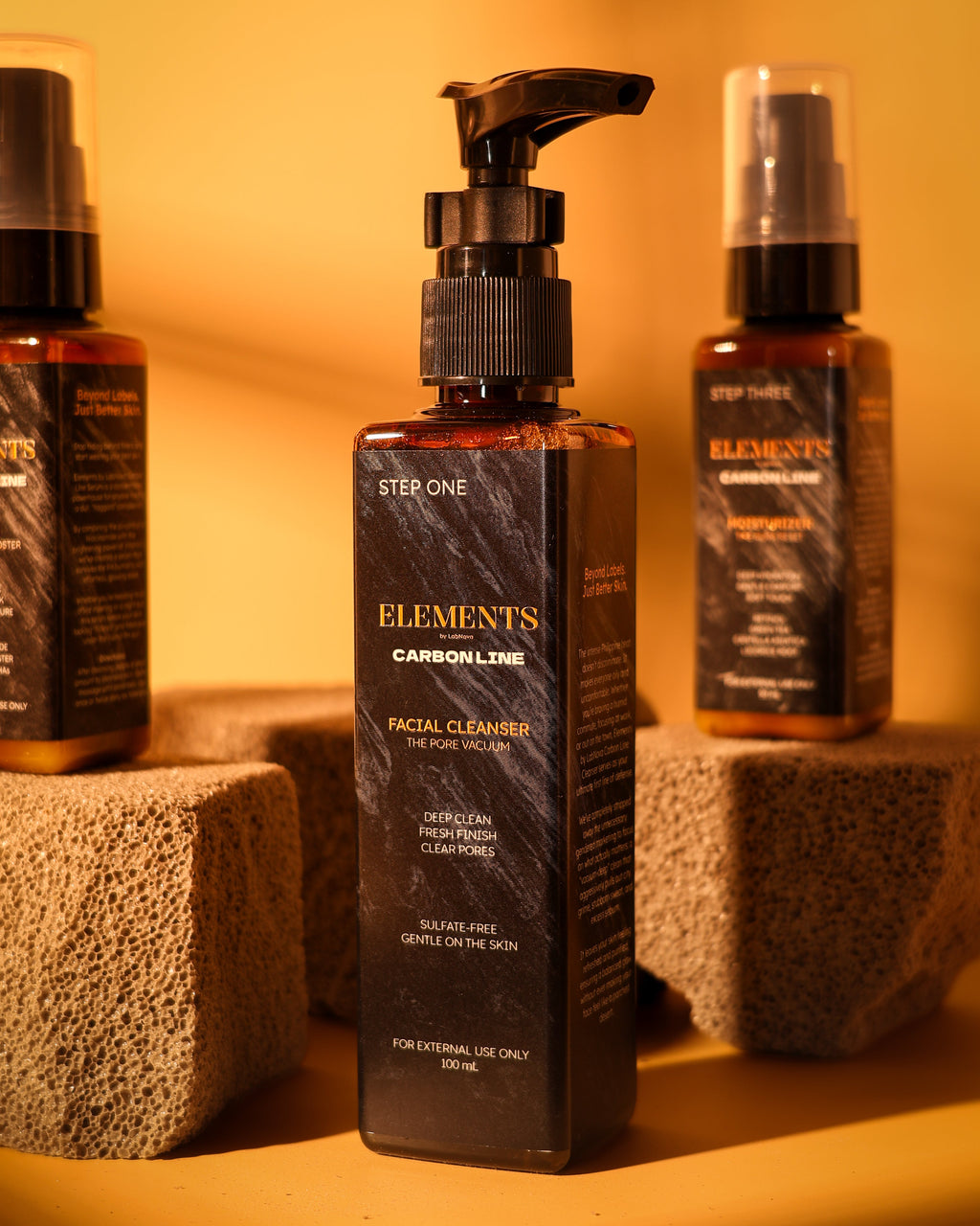 Three bottles of 'Elements' skincare products on a textured surface with a warm glow.