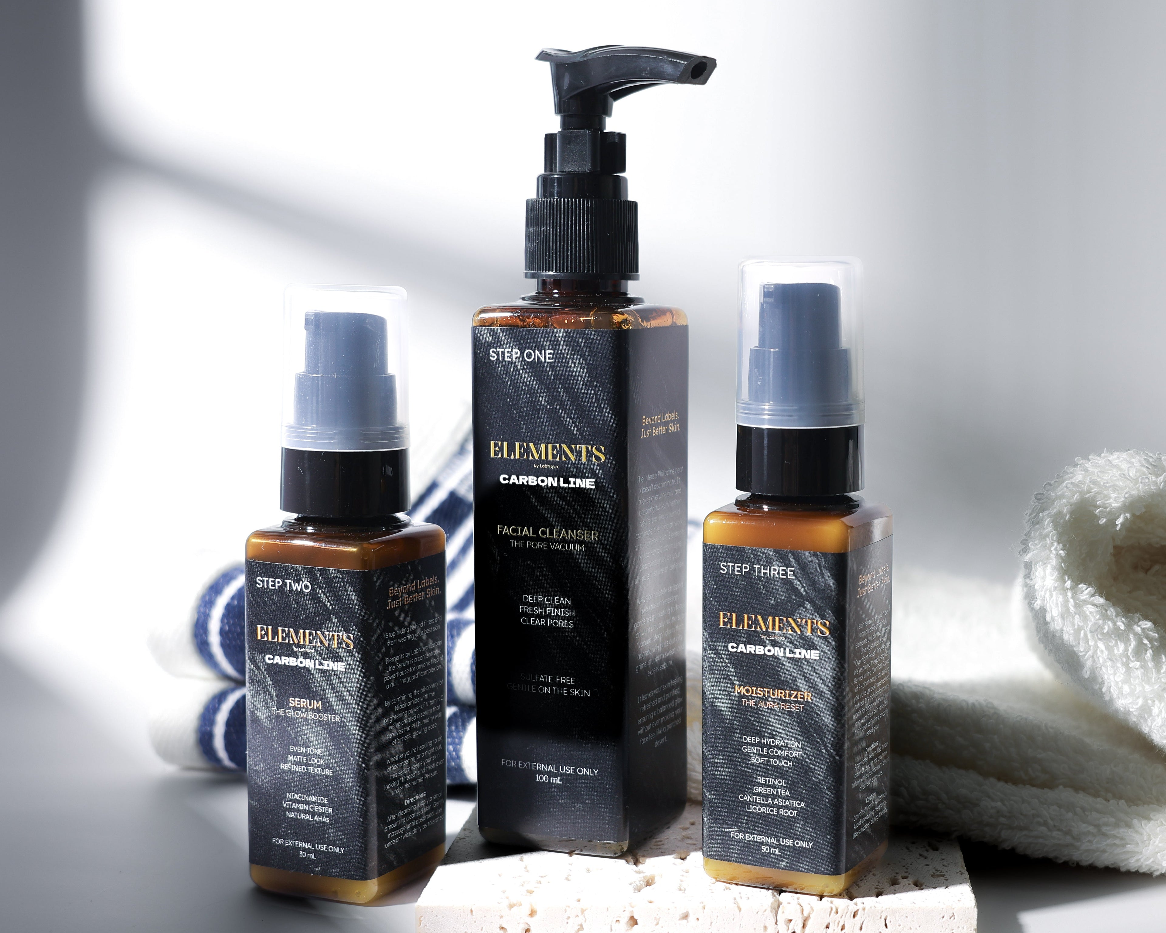 Three skincare bottles with pump and spray mechanisms on a white surface with a towel.