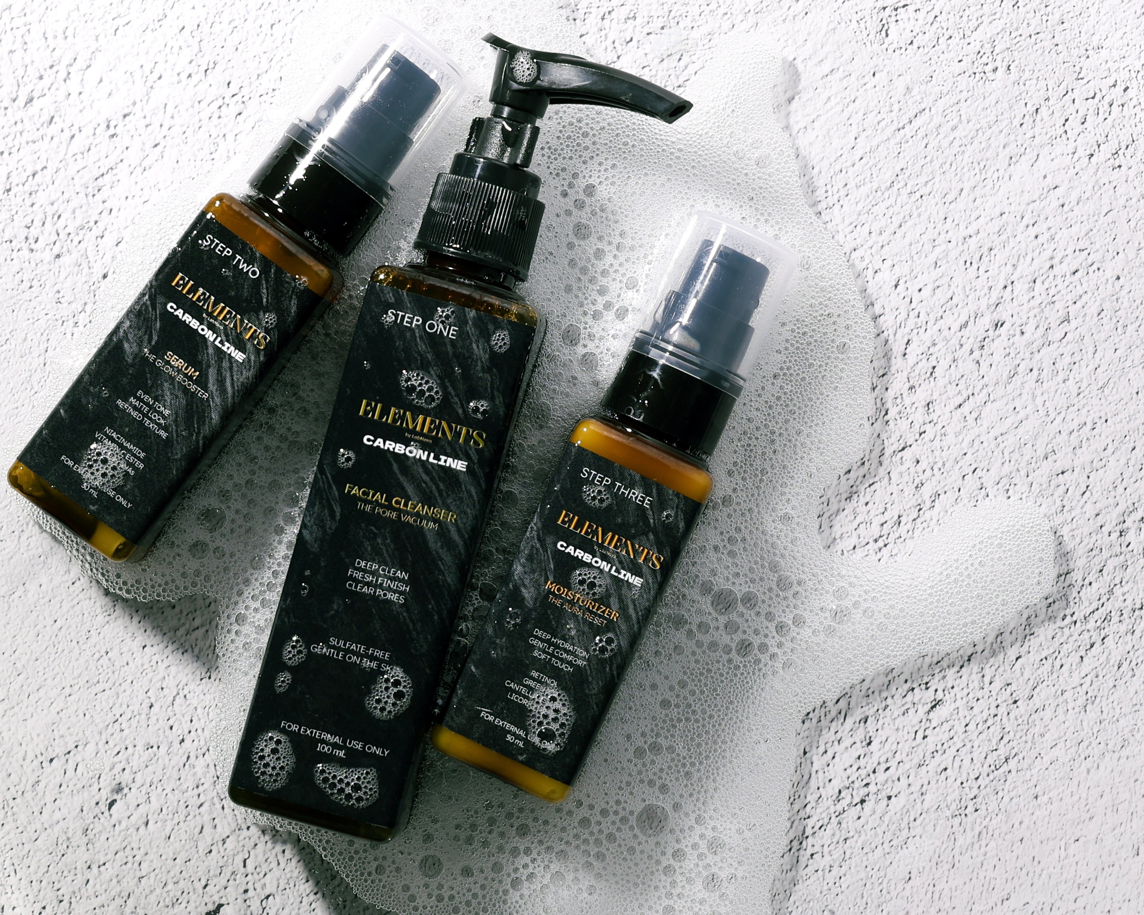 Three bottles of 'Elements' skincare products on a textured white surface.